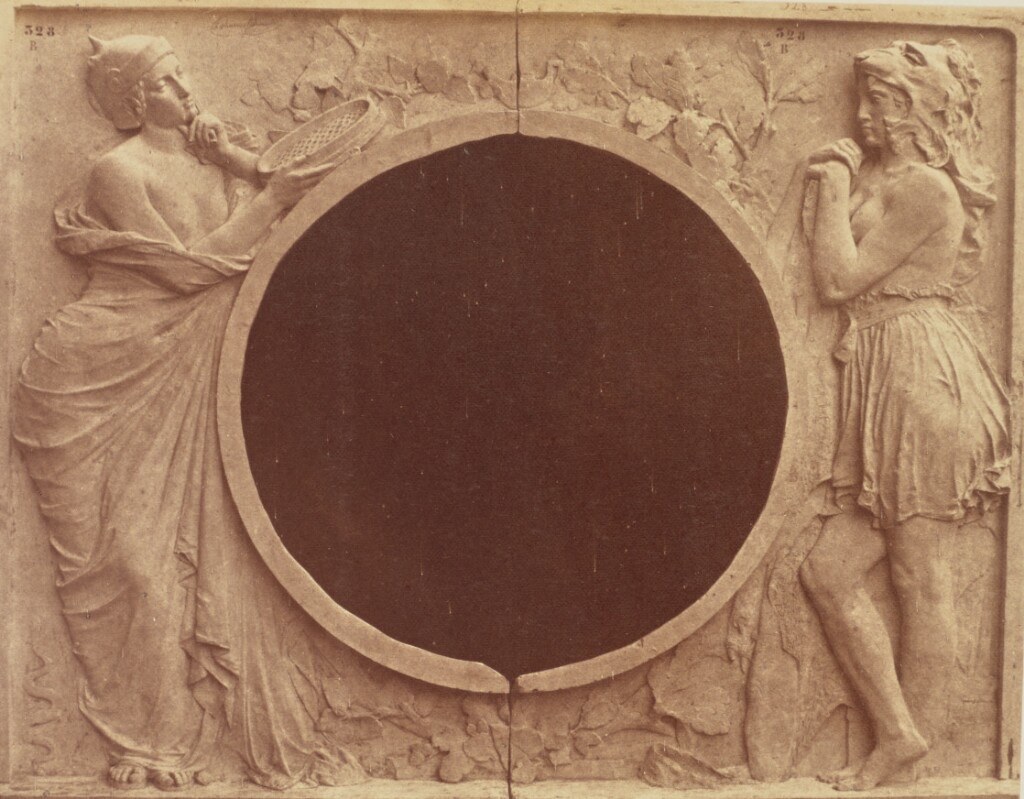 Historic sepia photograph of two sculpted female allegories, Justice holding scales and Fraternity standing opposite her, positioned around a large circular architectural opening.